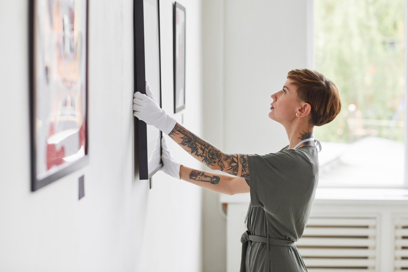 Creative Woman Hanging Paintings in Art Gallery